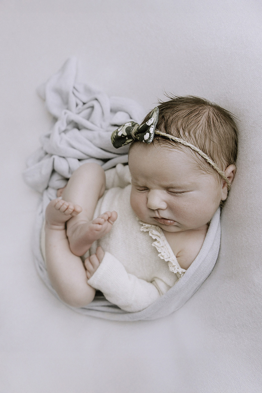 shooting d'une petite fille à sa naissance sur un fond uni avec un joli body en dentelle et laine
